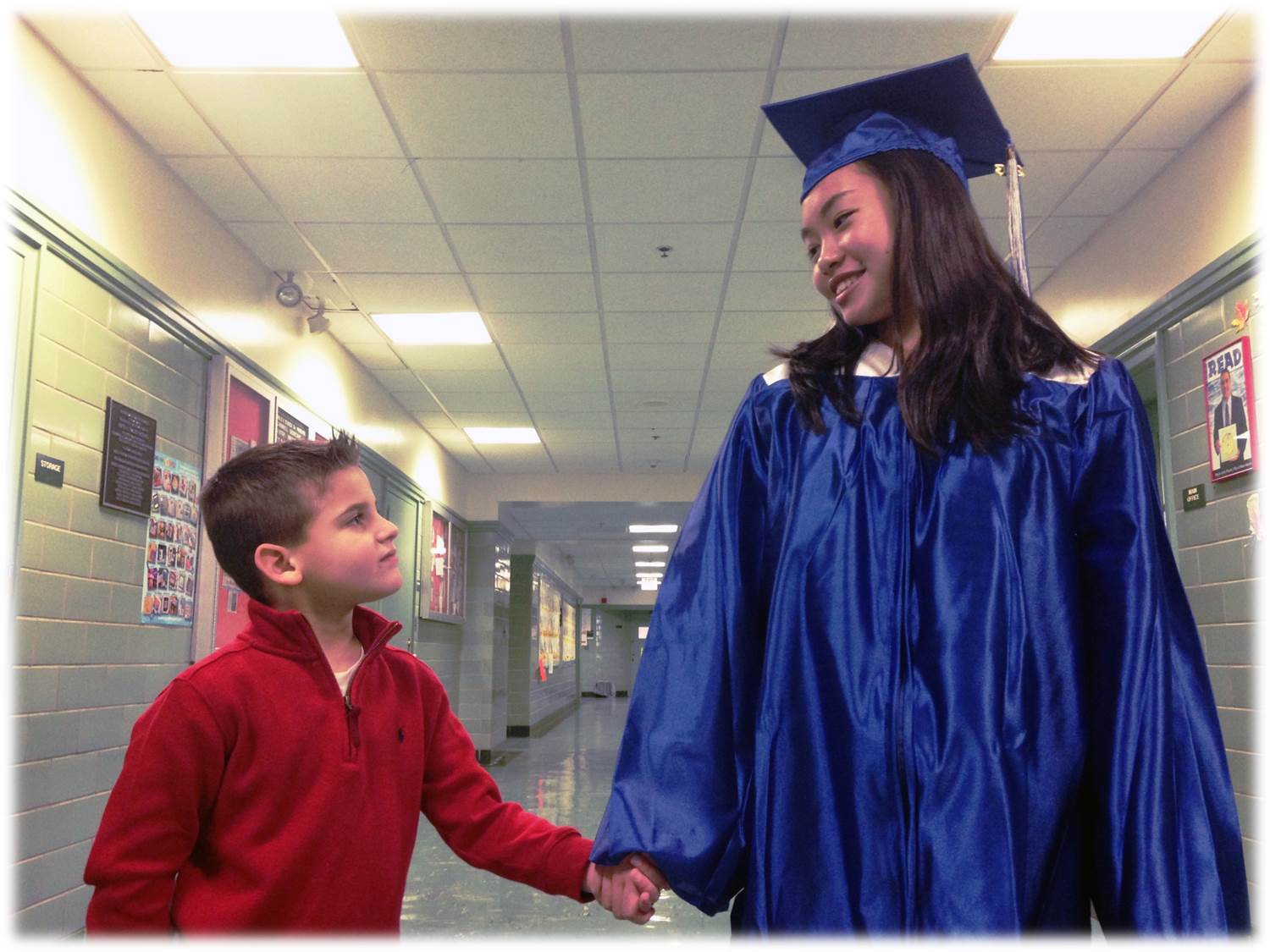 Elementary student walking with high school graduate