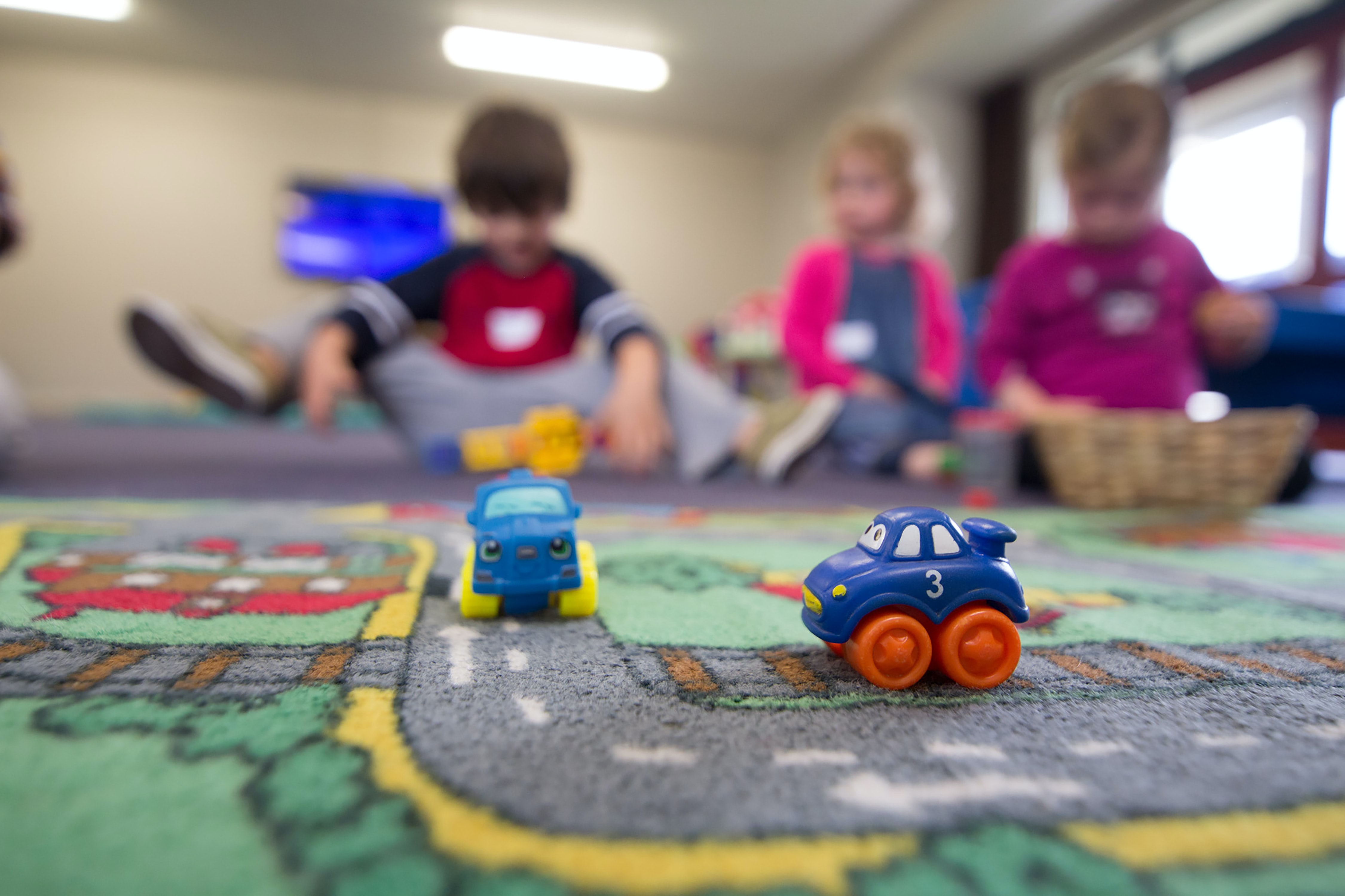 Three kids playing on a rug with trucks