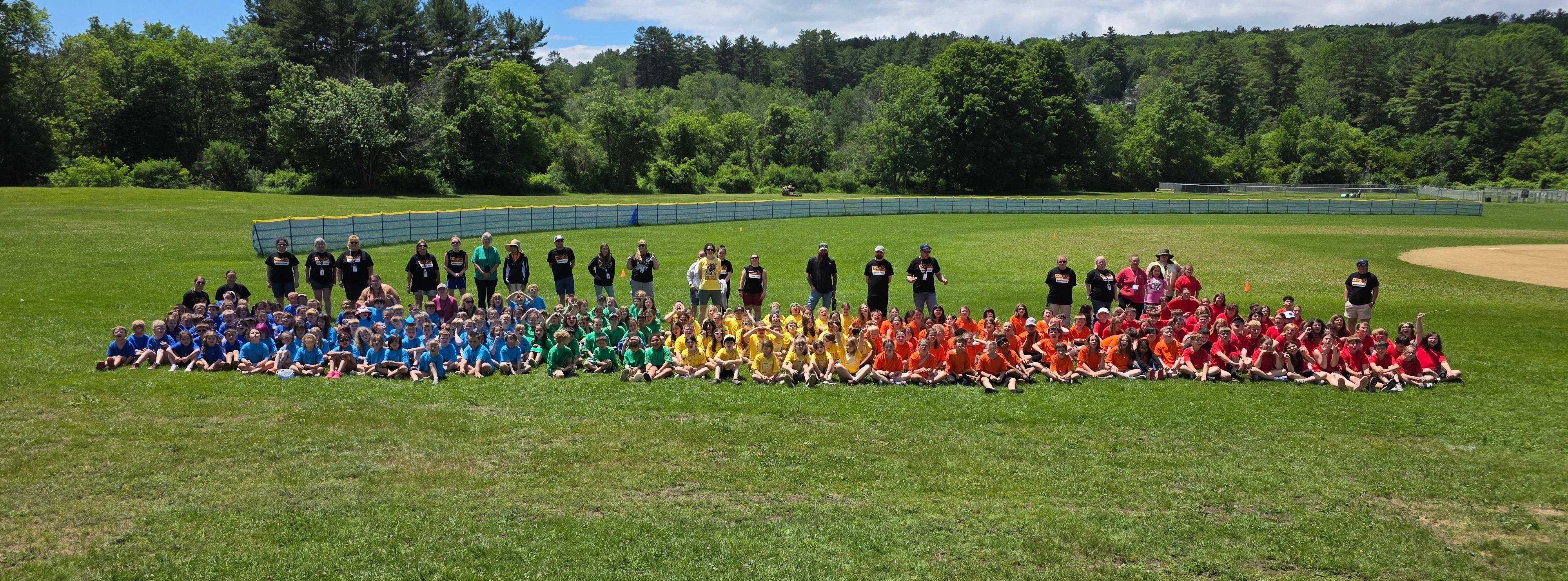 group of students wearing rainbow colored shirts sitting in a field during field day