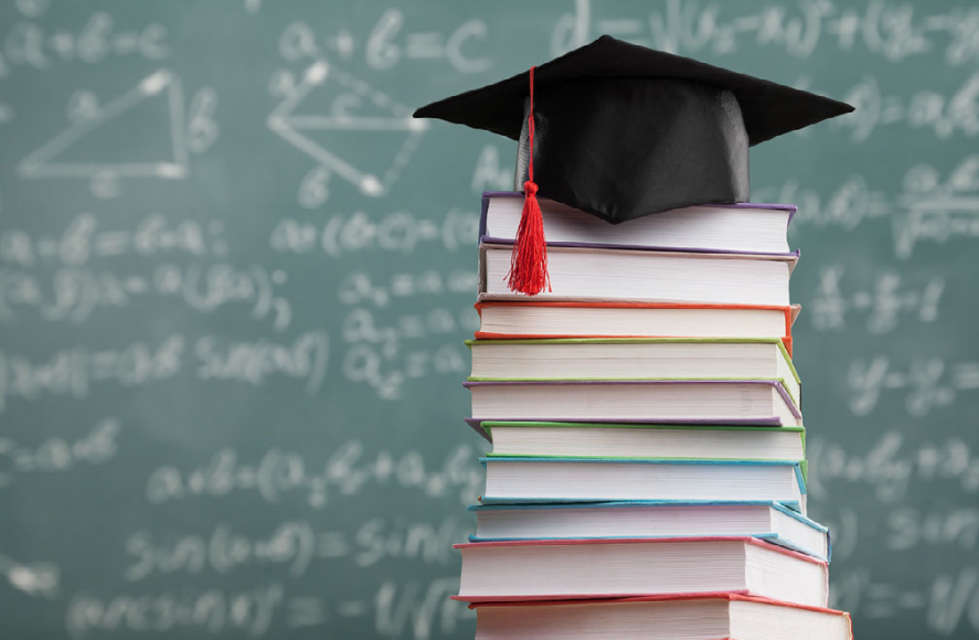 Graduation cap on books in front of chalkboard