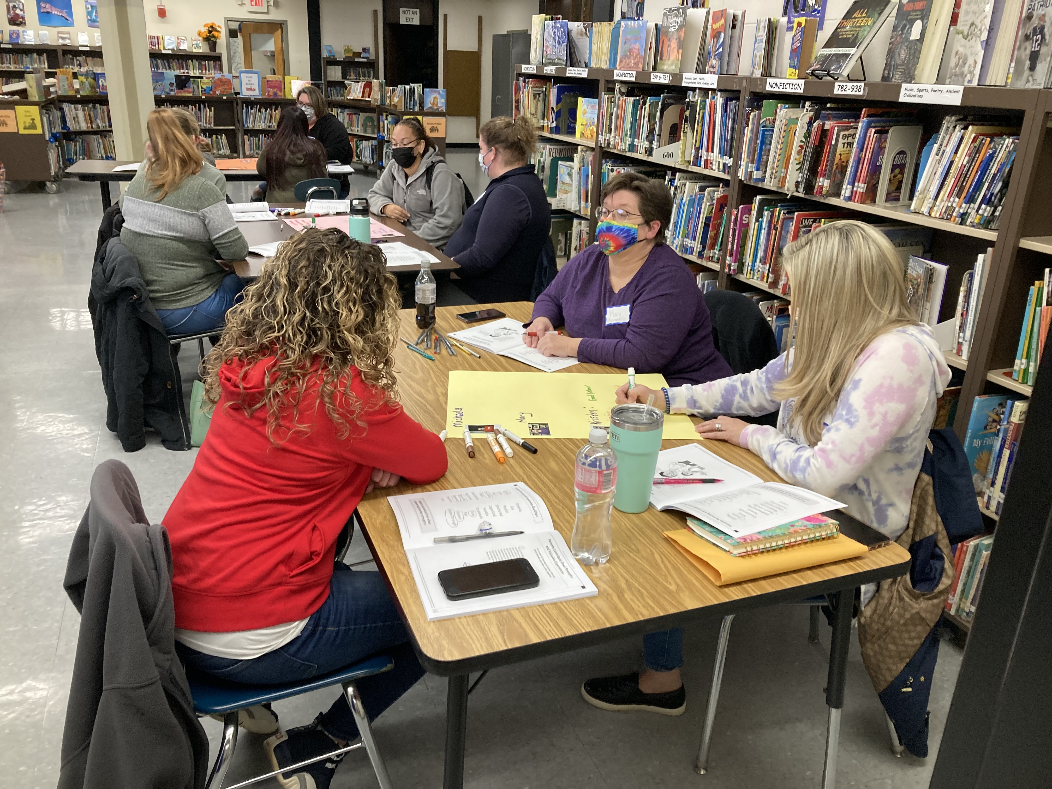 adults in discussion at tables in the school library