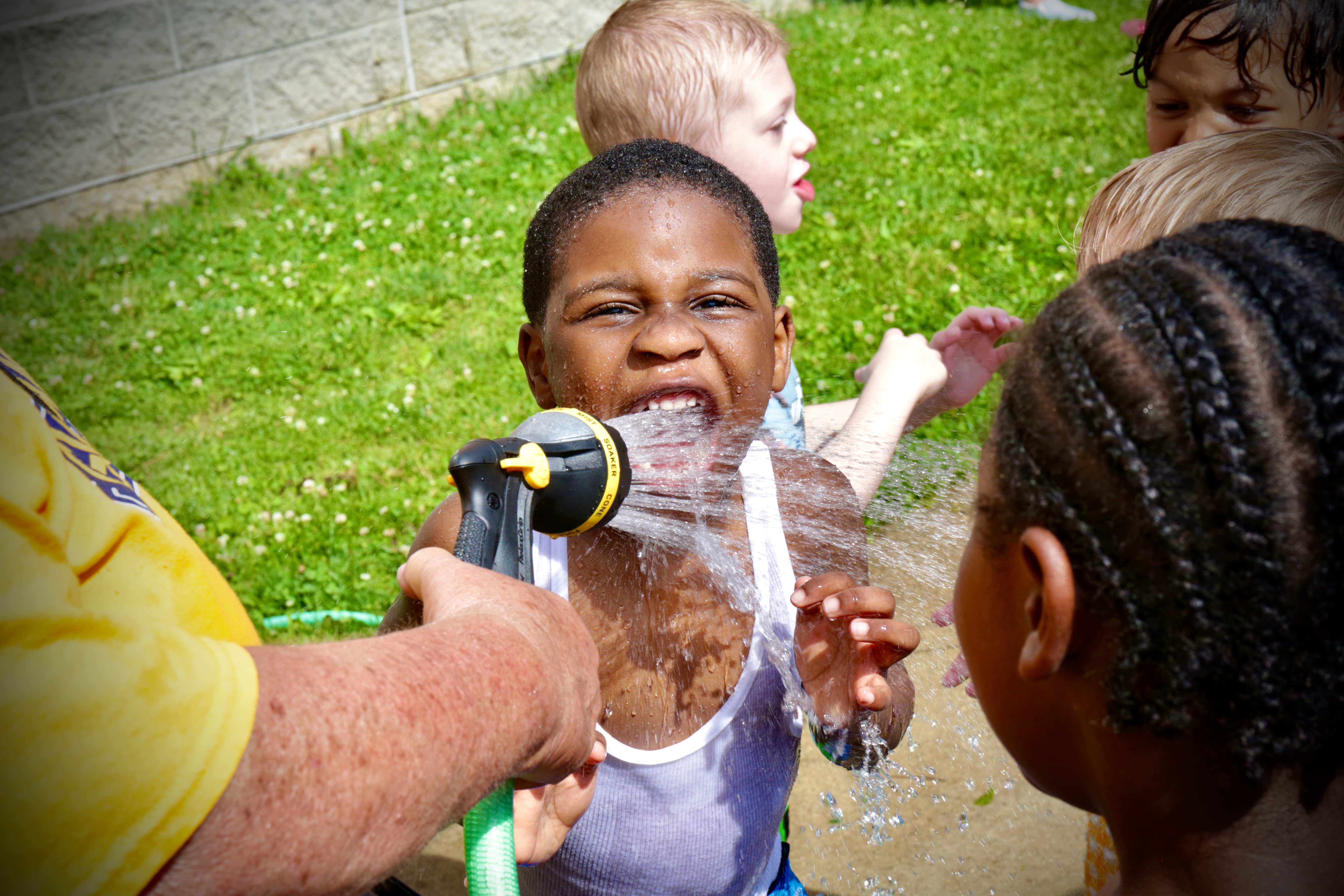 A Clark Preschool student enjoys a drink from a garden hose during outside playtime