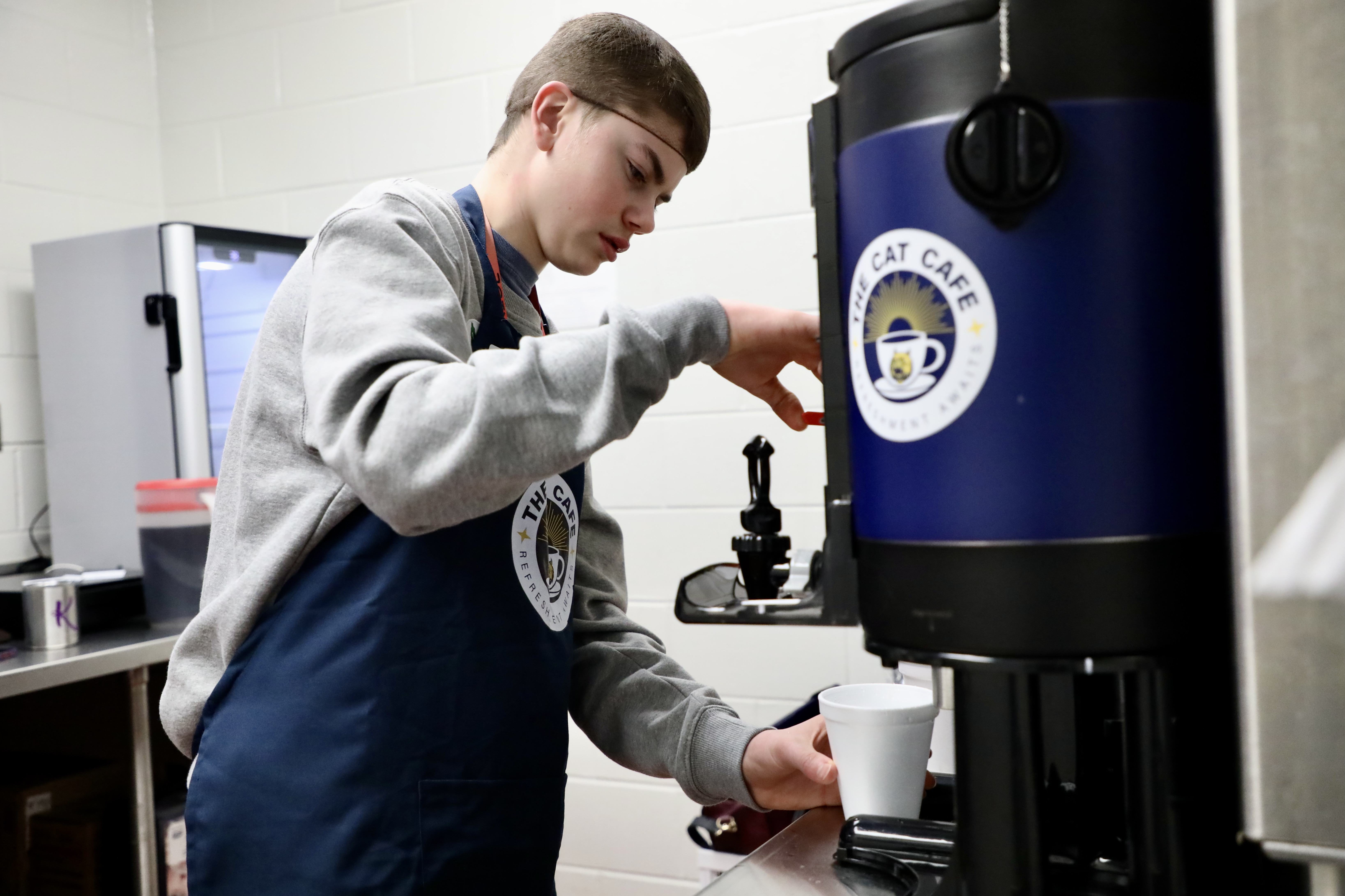 A student pours coffee from a machine in the Cat Cafe