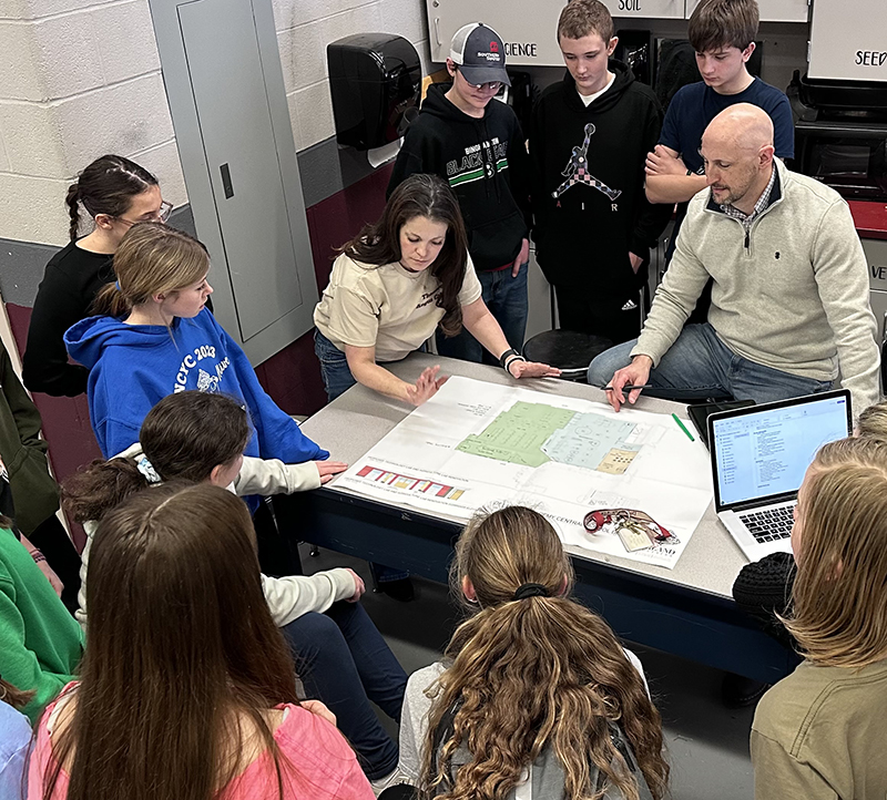 two adults and a number of students reviewing planning drawings