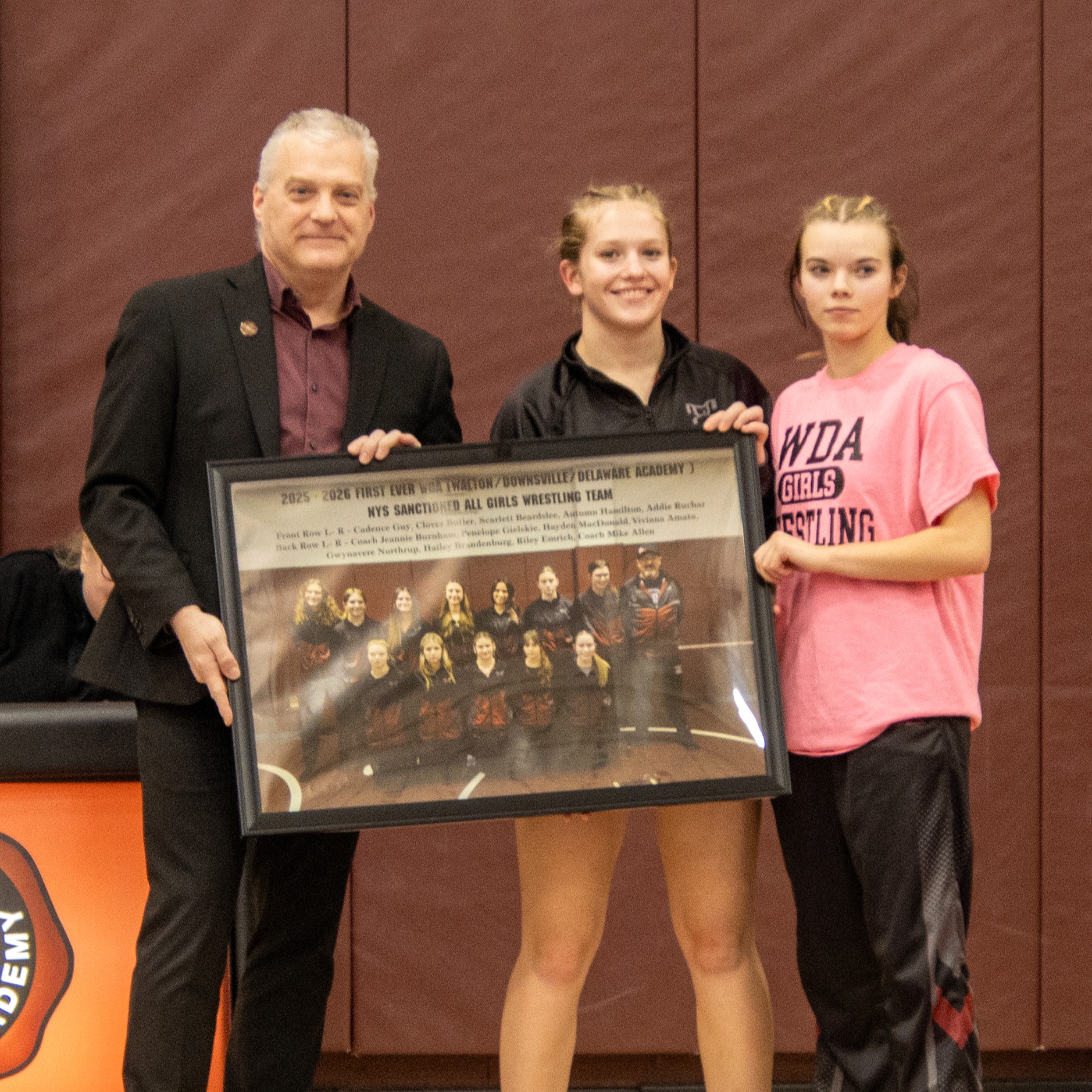 Mr. Shultz receives a framed photo of the girls wrestling team from two wrestlers