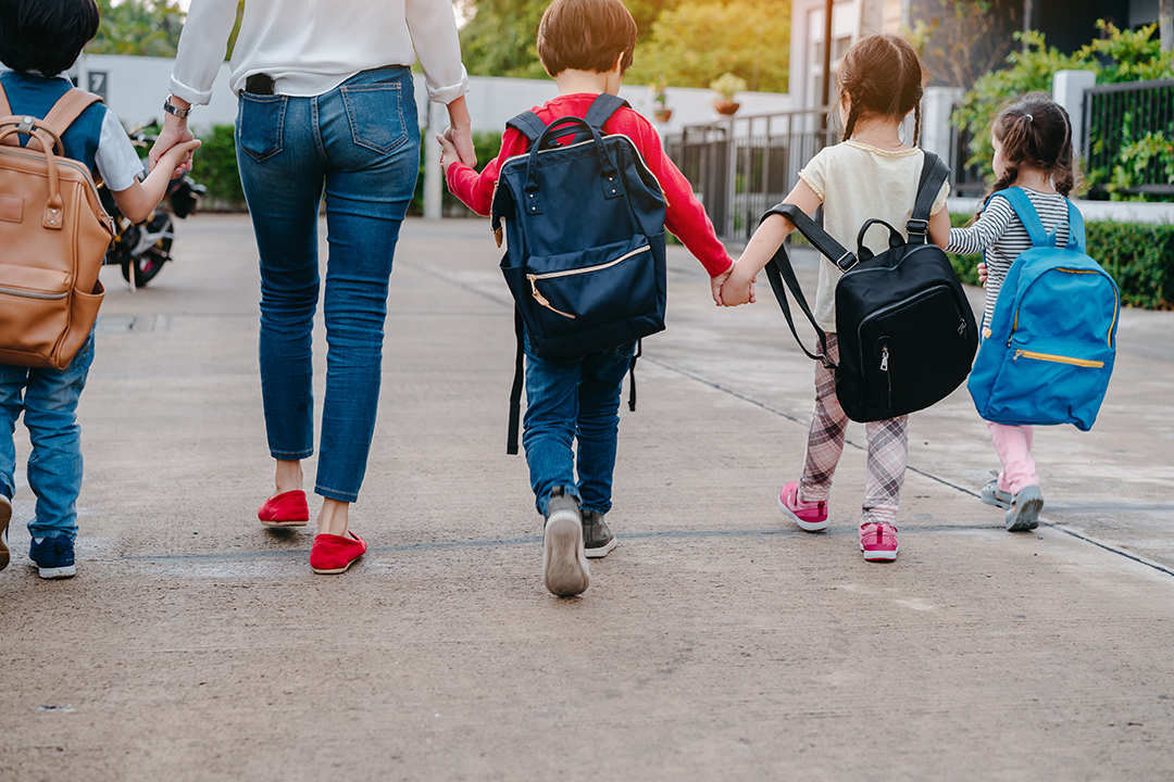 Parent holding hands of students with backpacks on the way to school