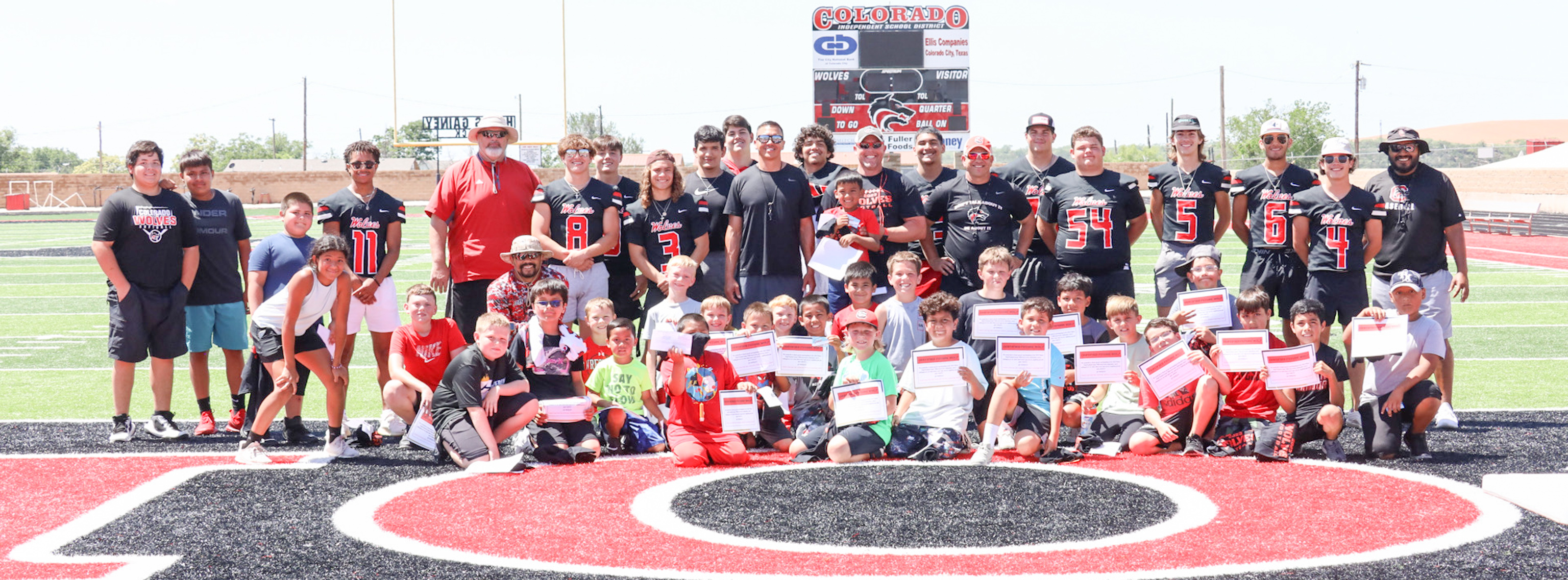 Group of young kids pose with coaches and varsity players at football camp