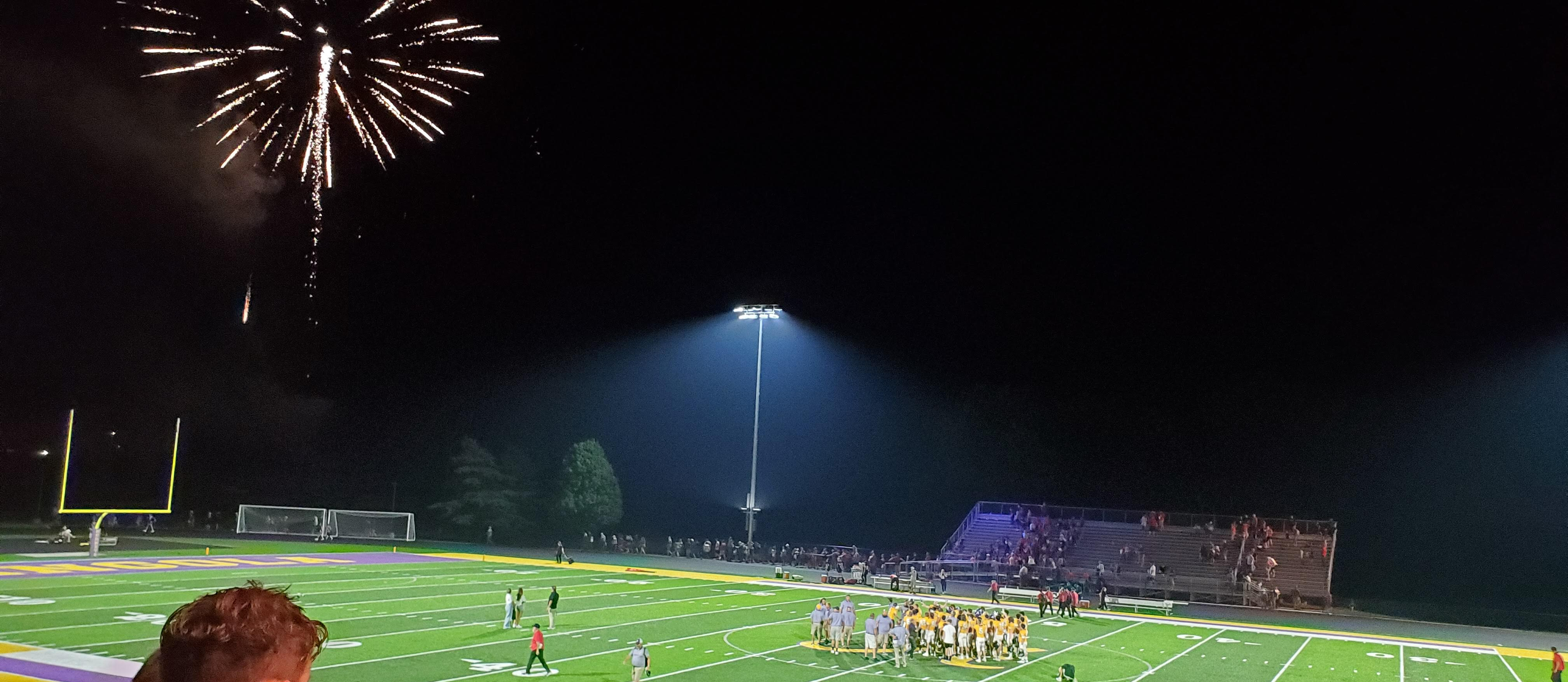 Lights on the football field, the team celebrating, and fireworks in the sky