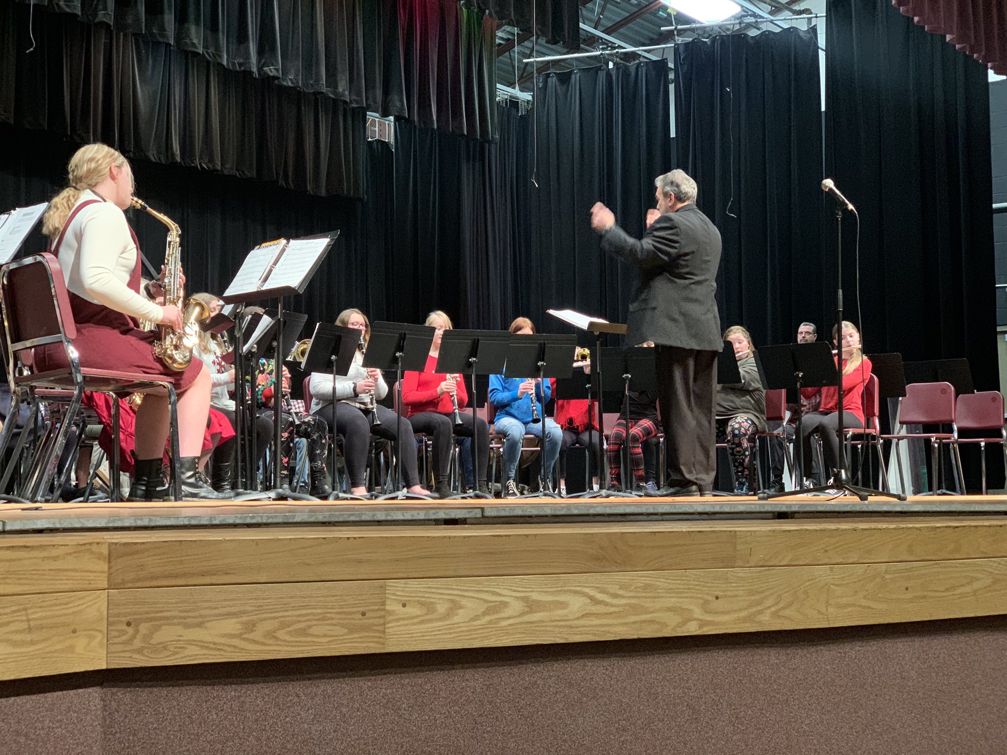Students play a band concert on the stage with the band director leading them.