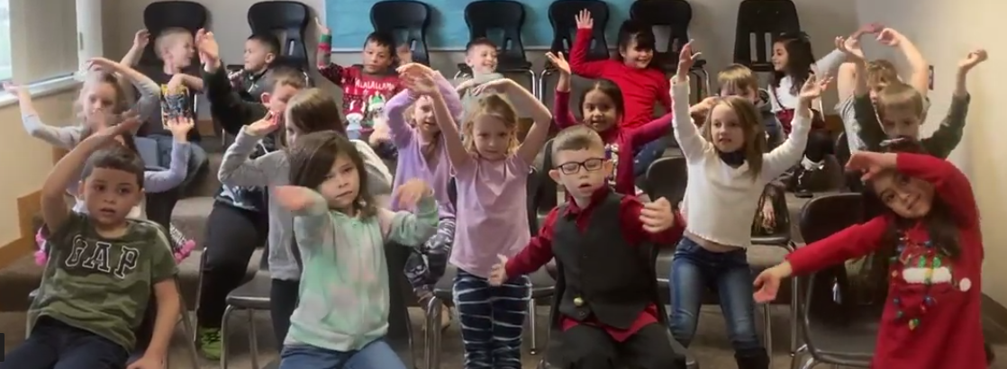 Students sit in chairs in music class waving their arms side to side in the  air