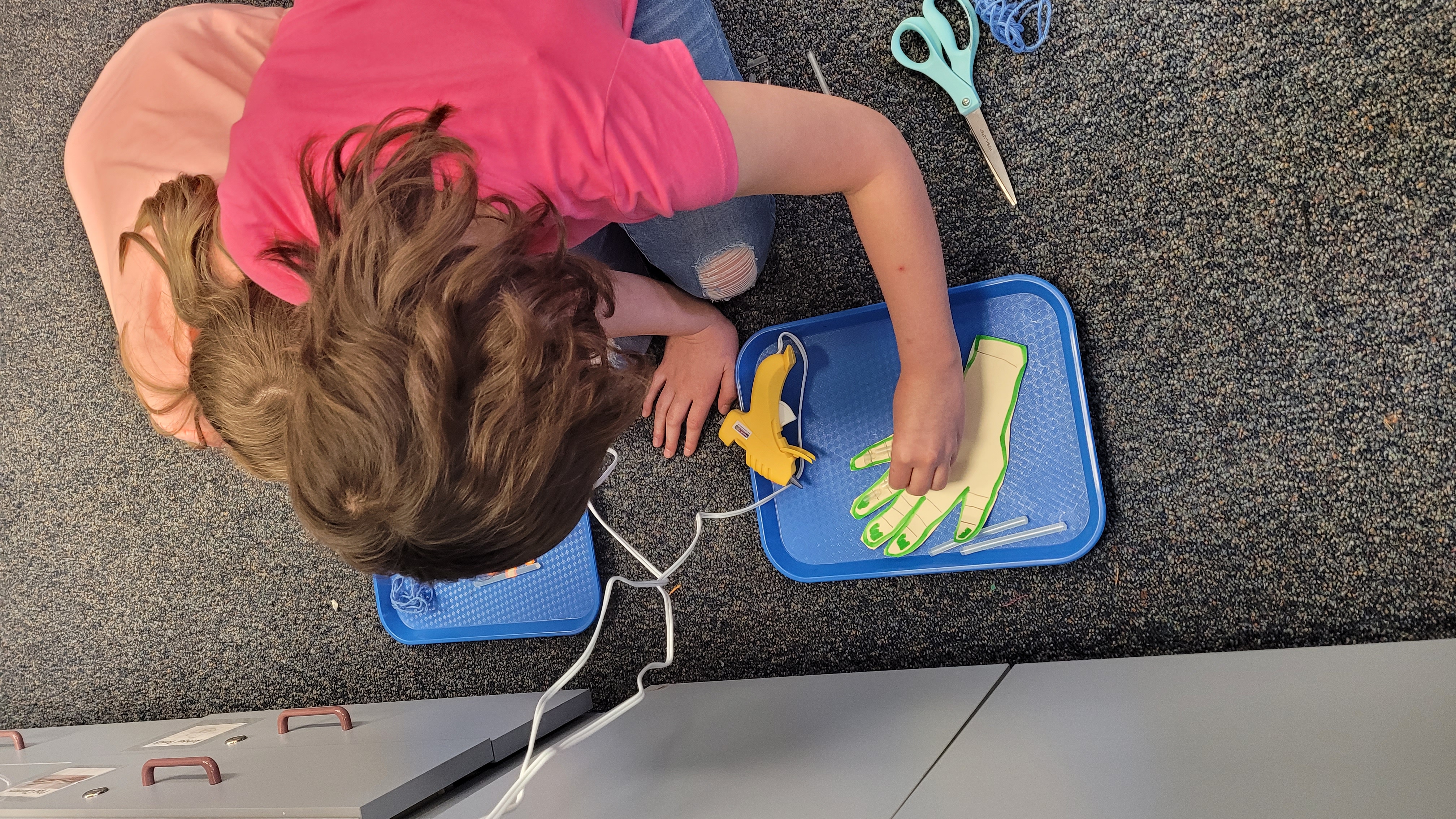 A student works on a handprint art project with a hot glue gun and scissors