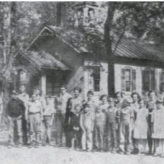 Black-and-white photo of a group of people in front of a small house with trees.