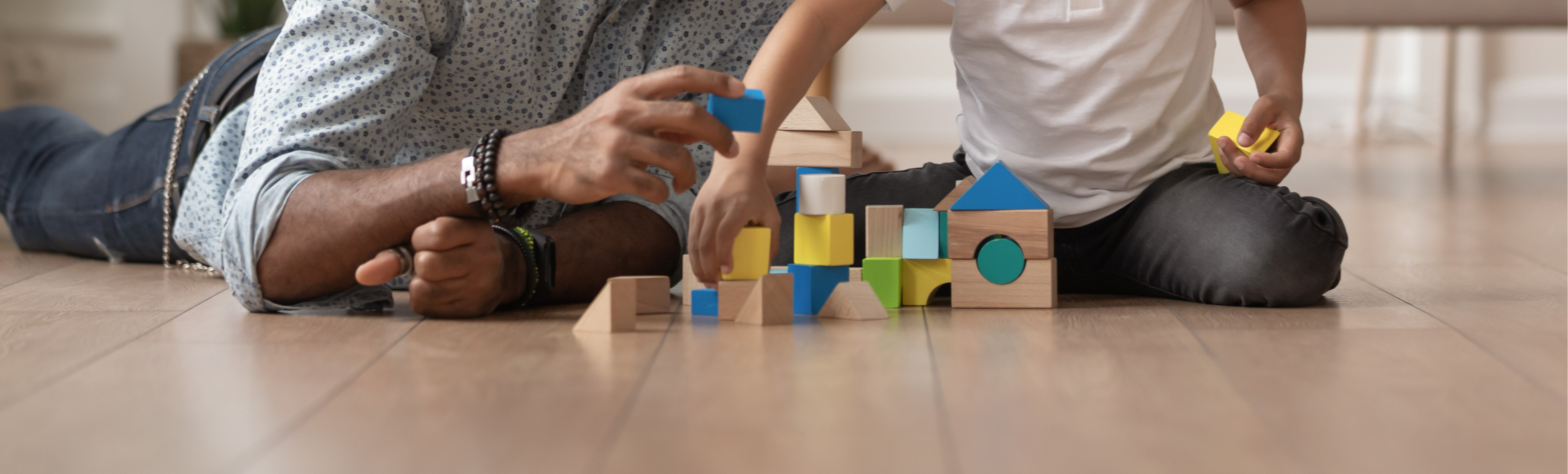 A cropped picture showing a father and his child playing with toy building blocks.