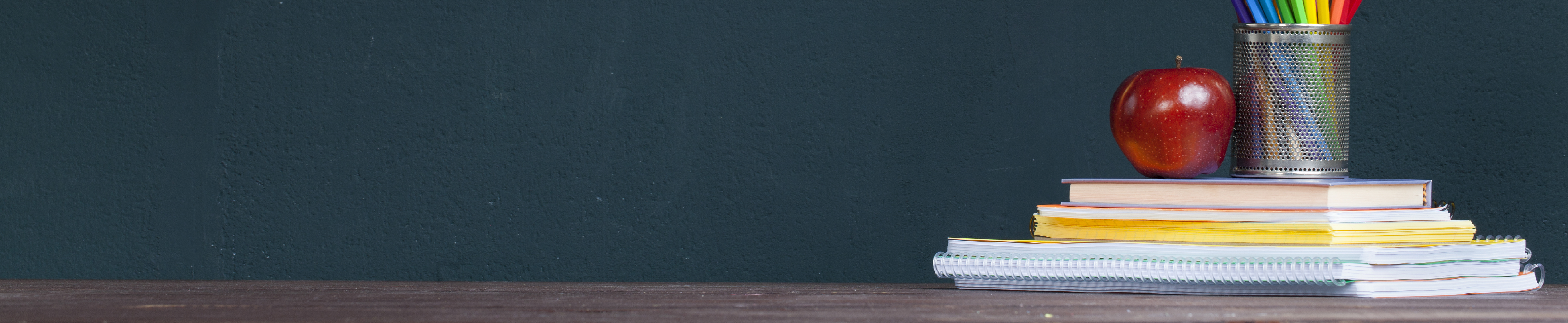 An apple on top of a stack of books in front of a blackboard.