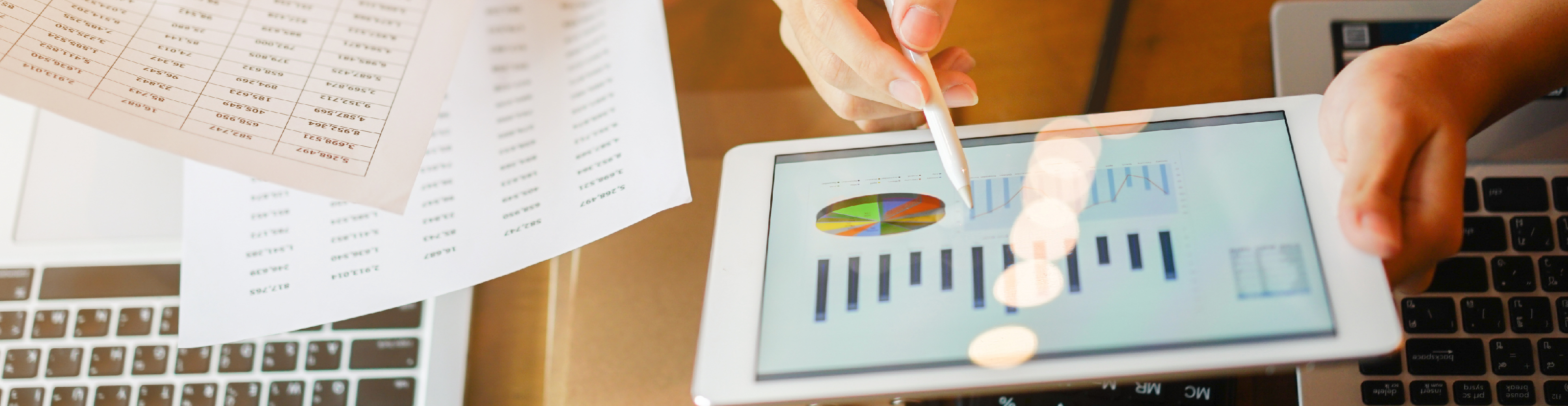 Hand holding tablet with piechart and bargraphs on it, and compared it against tables printed out on paper