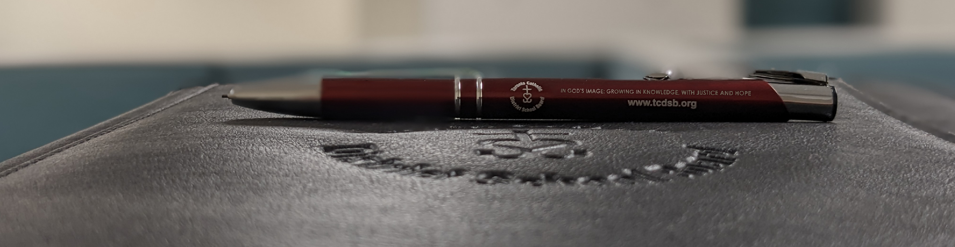 Red TCDSB branded pencil lying on top of TCDSB branded black folder.