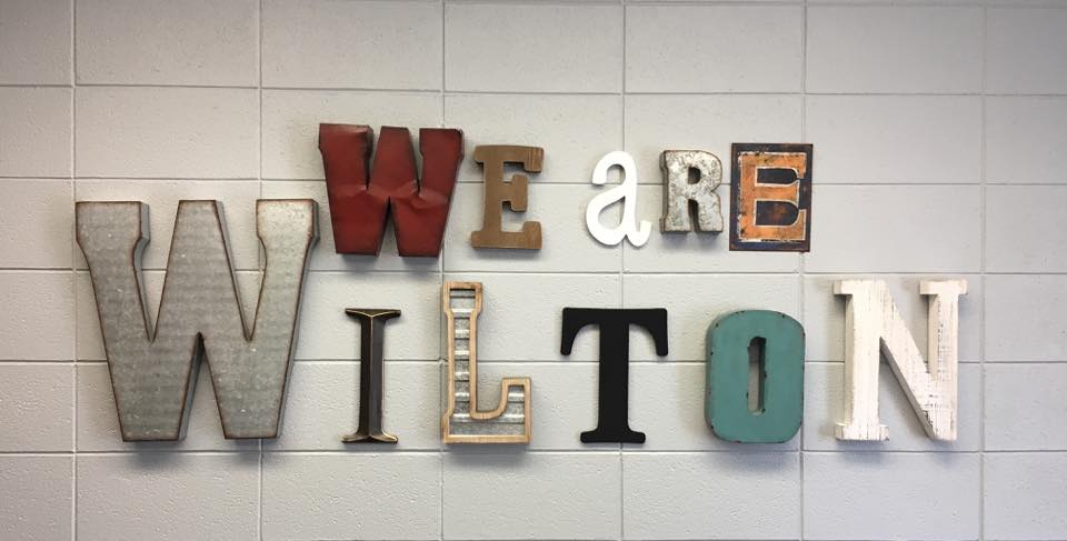 we are wilton in wooden letters on white brick wall