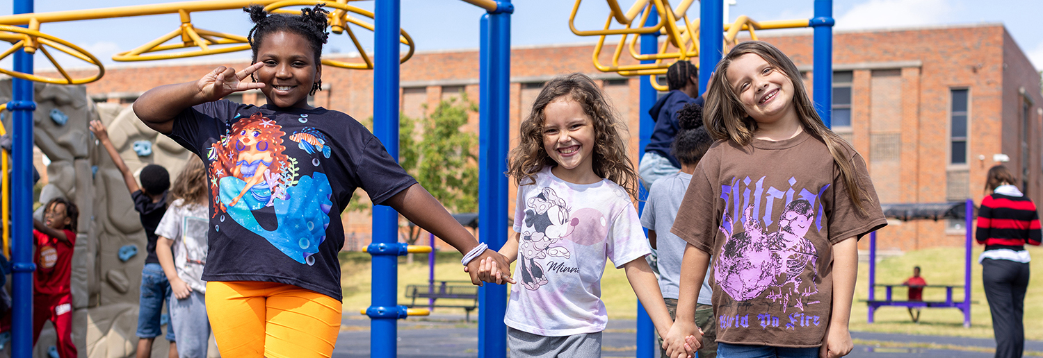 Three girls hold hands on the Center Elementary playground.
