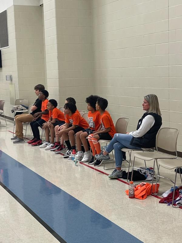 a coach sits on the sidelines in chairs with her team on the basketball court