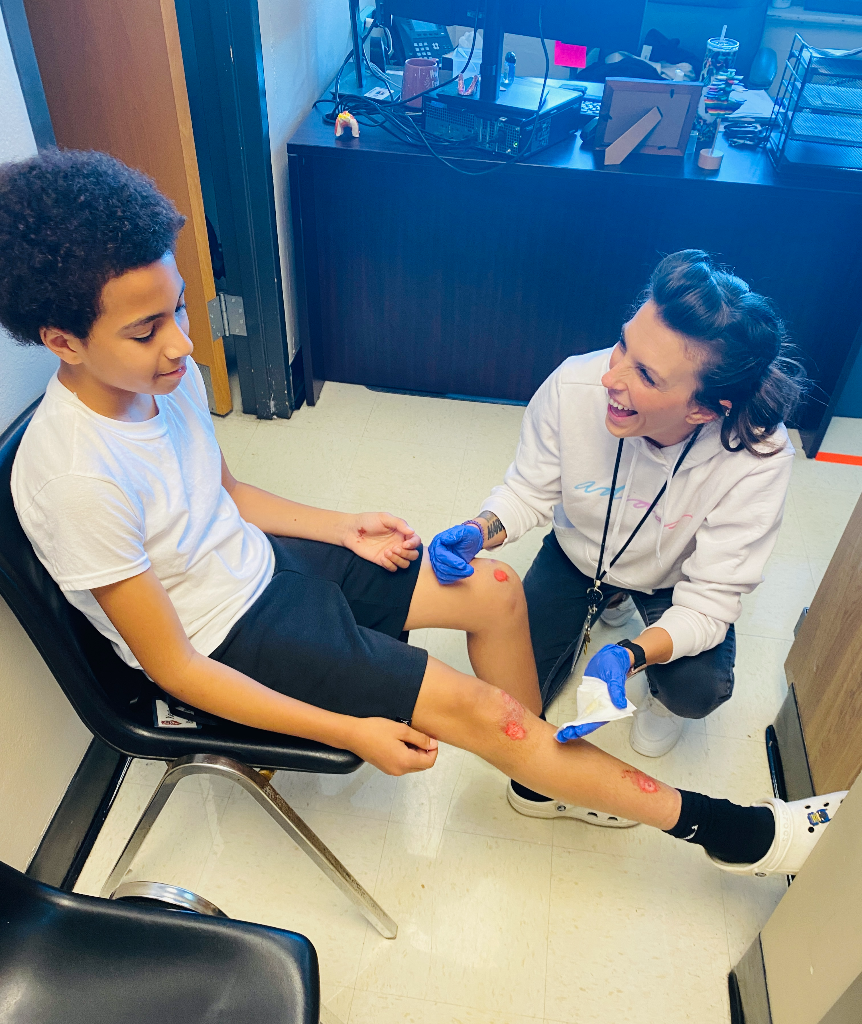 a nurse smiles as she helps a student with wounds on his leg