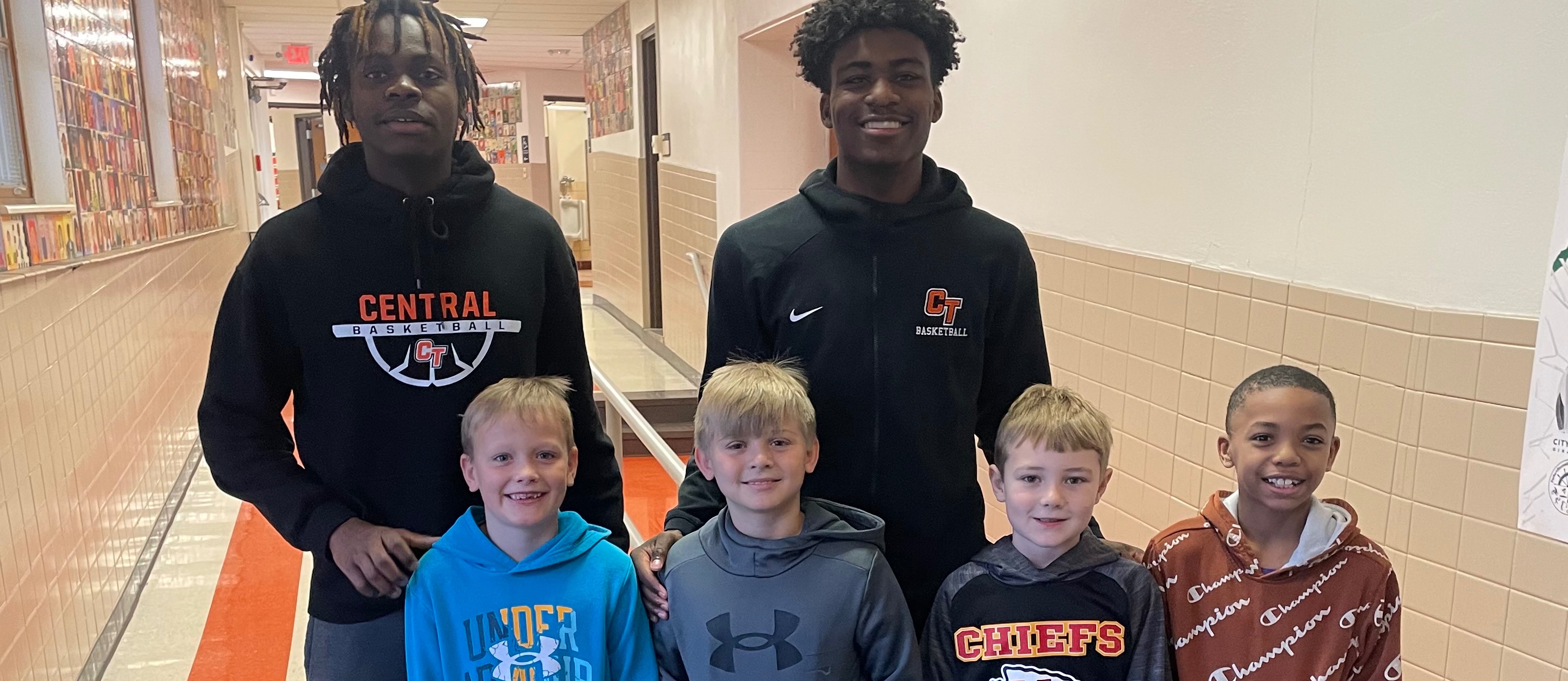 Two high school basketball players post for pictures with elementary students