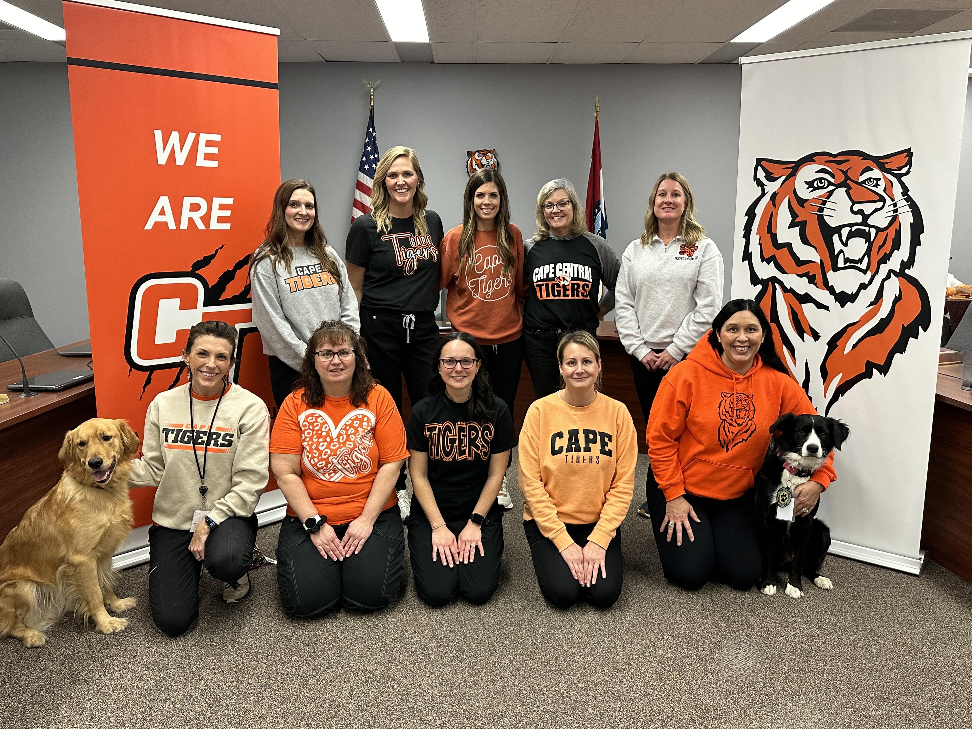 Ten school nurses standing in front of a sign that says home of the tigers, smiling for a picture 