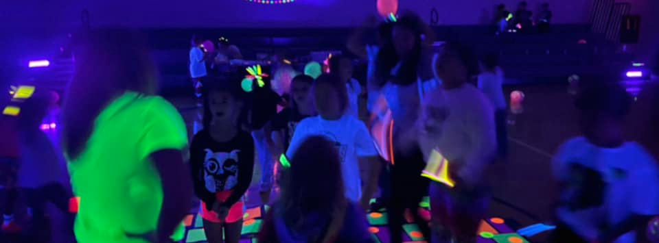 students dance in the gym at a glow party