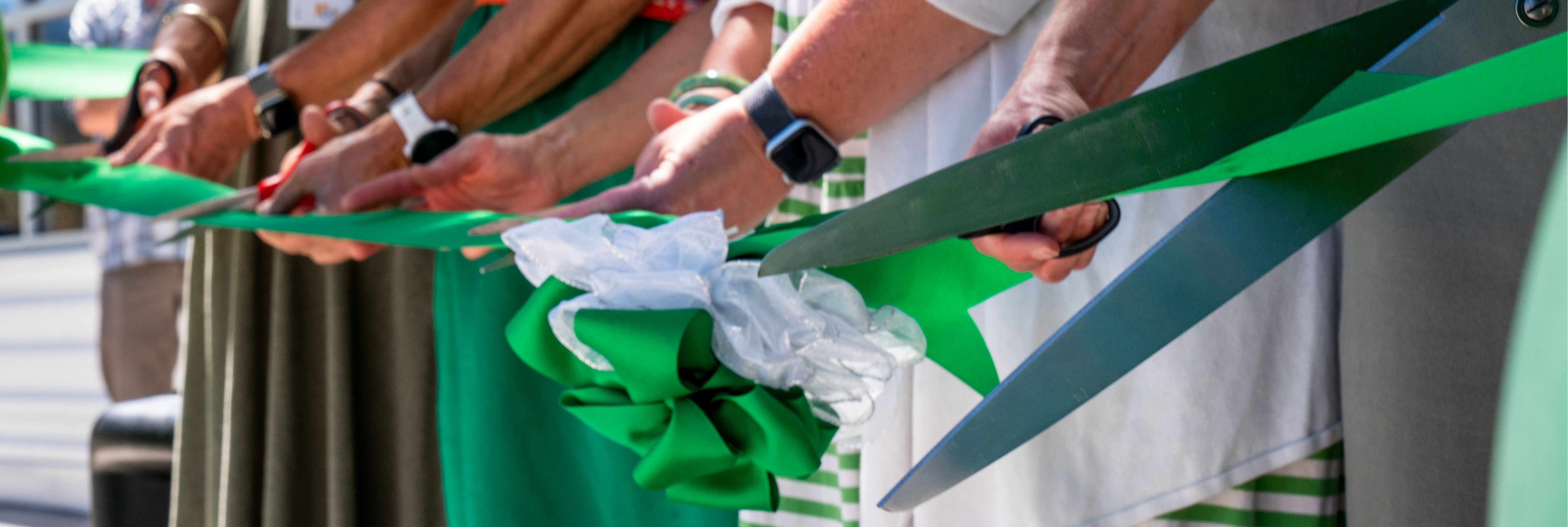Hands holding scissors cutting green ribbon
