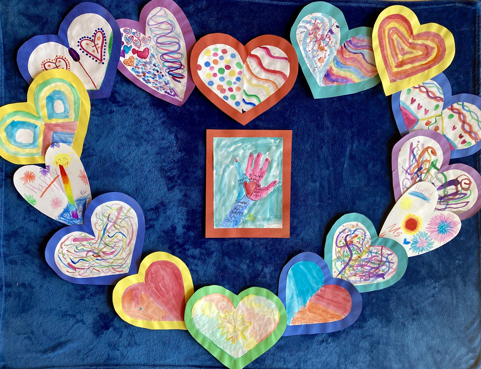 Colorful student-made heart drawings displayed in a circle around a central artwork.