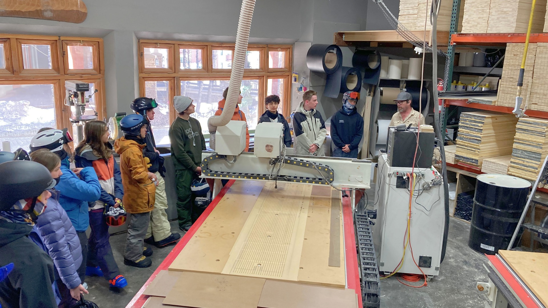 Students in a workshop with a large machine and wood materials.