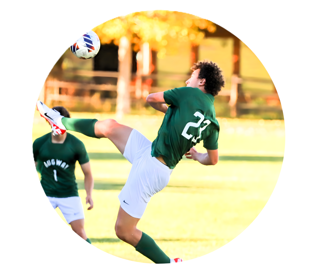 Soccer player in green uniform kicking ball during a game while teammate watches nearby.