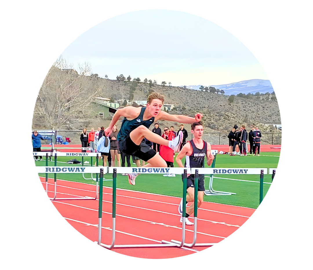 Track athlete clearing hurdle during race with competitor running nearby.