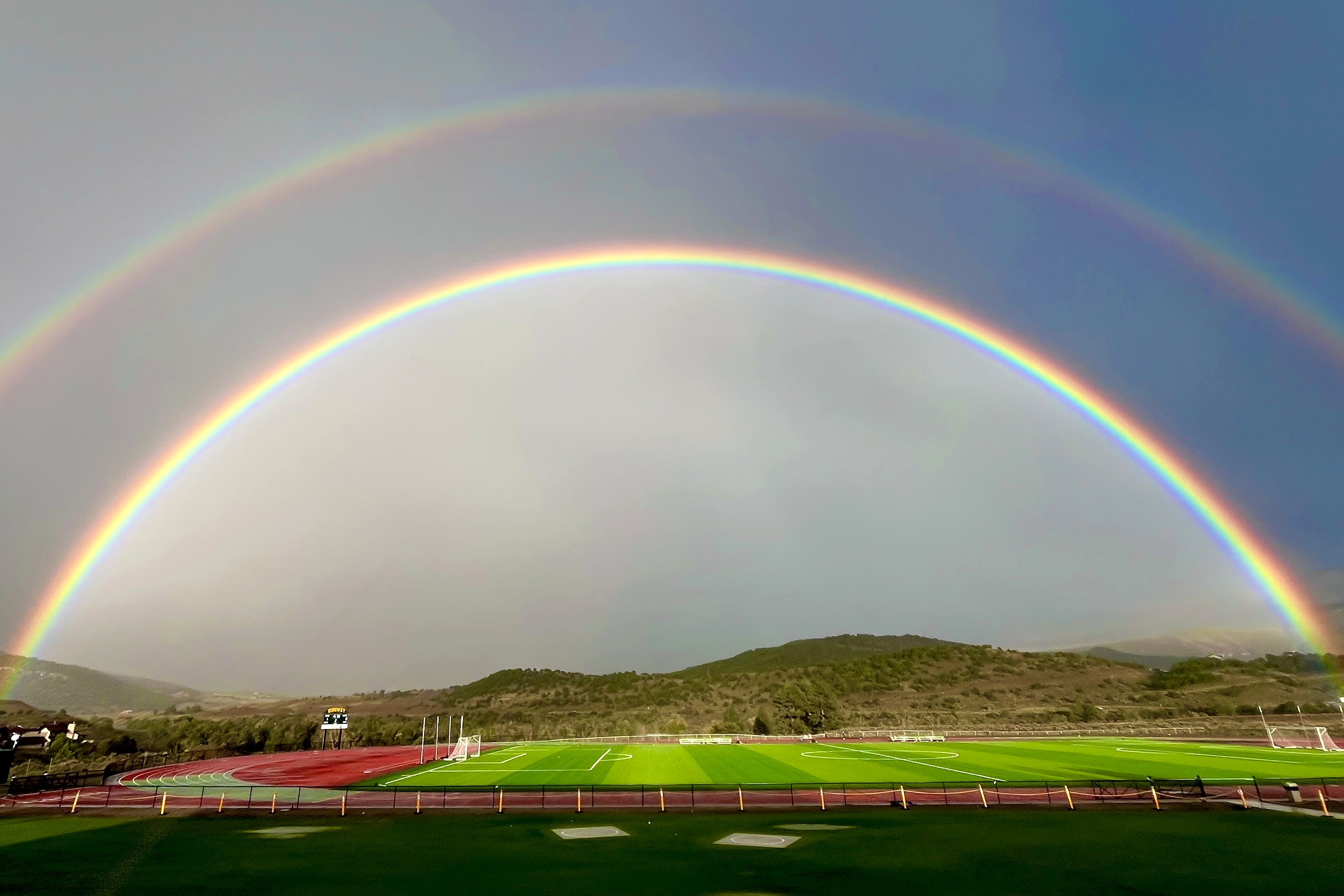 Double rainbow over the Cimarron Athletic field with track and hills in the background.