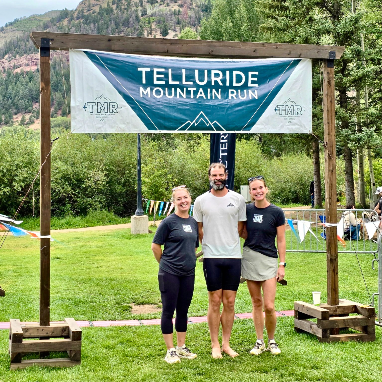 Three participants pose beneath the Telluride Mountain Run banner with mountains in the background.