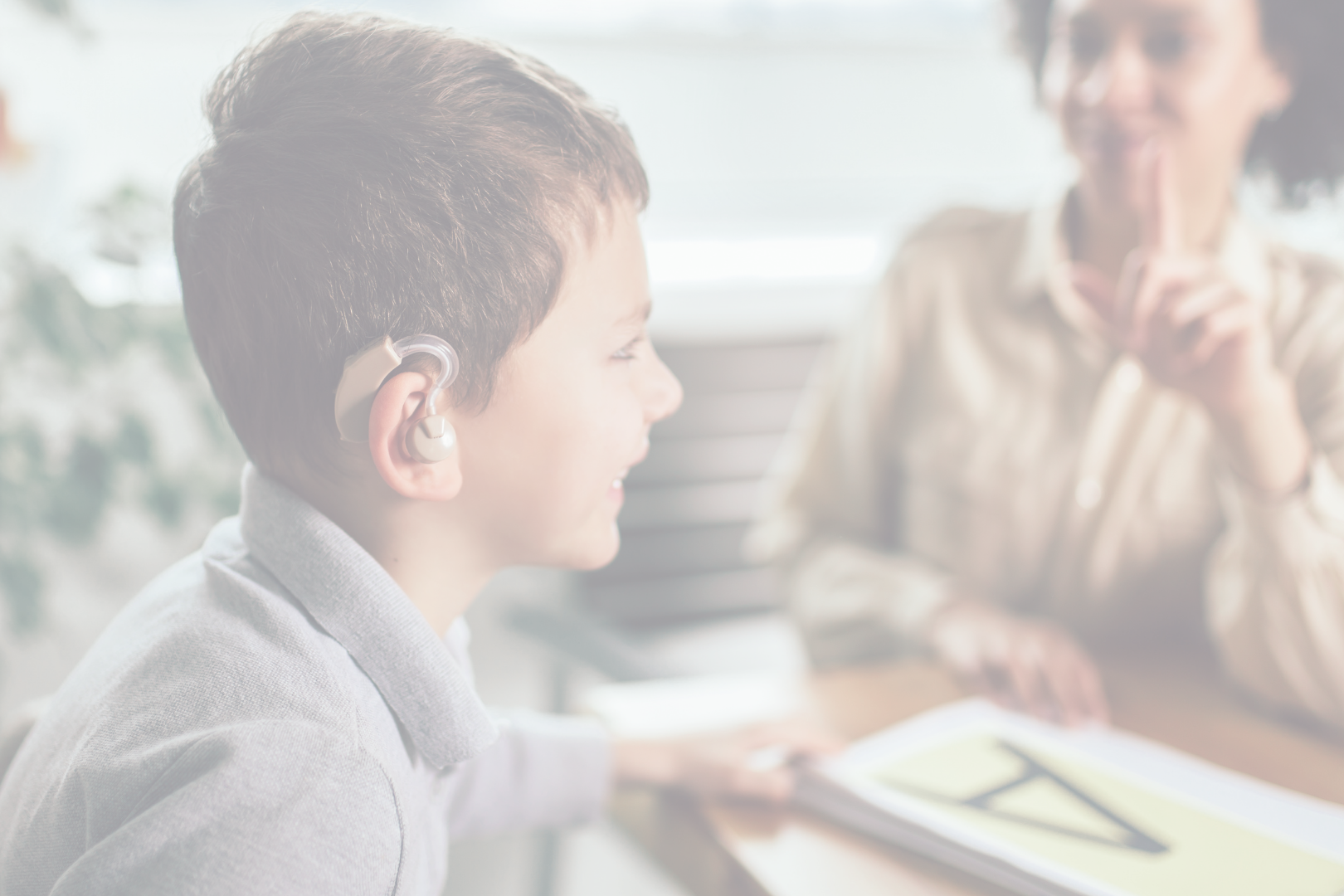 picture of elementary-aged male student with hearing aid being signed to by teacher