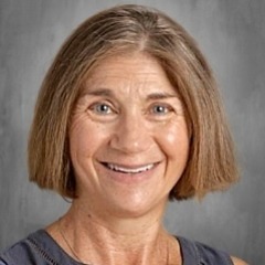 An adult woman with short, light-colored hair smiles in a studio with a gray background.