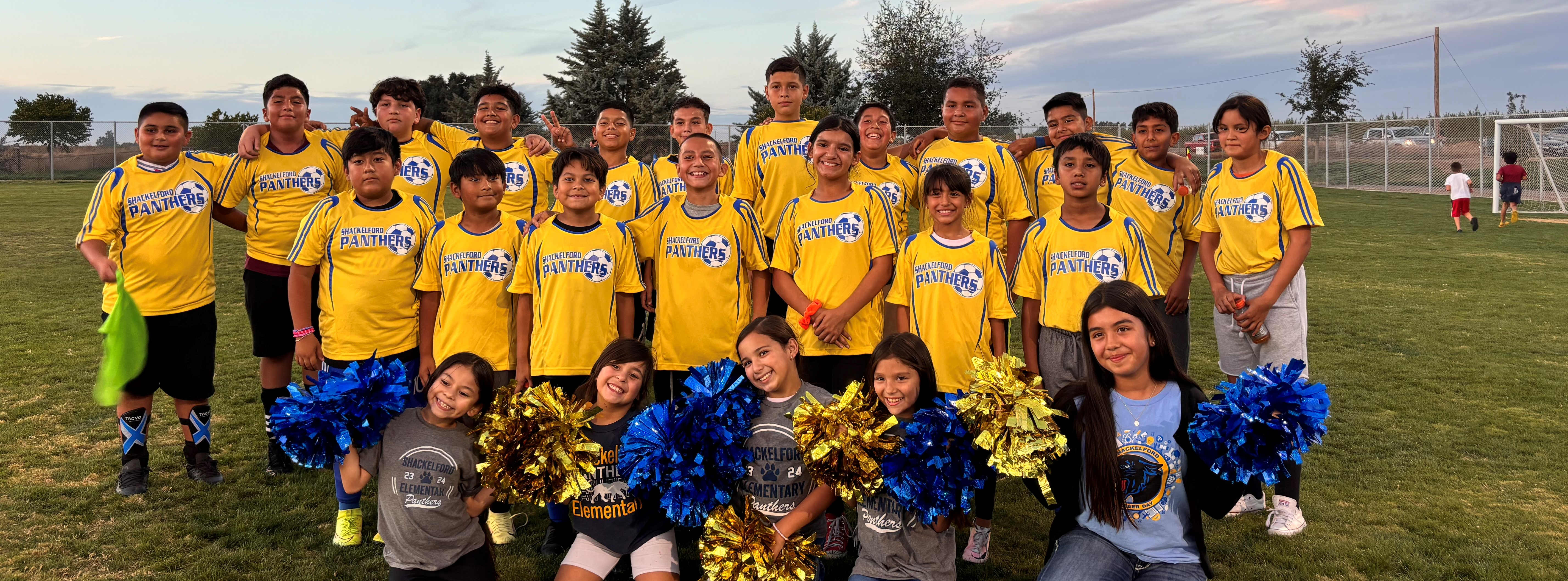 ELP Soccer team group picture with yellow jerseys and cheerleaders with pom poms