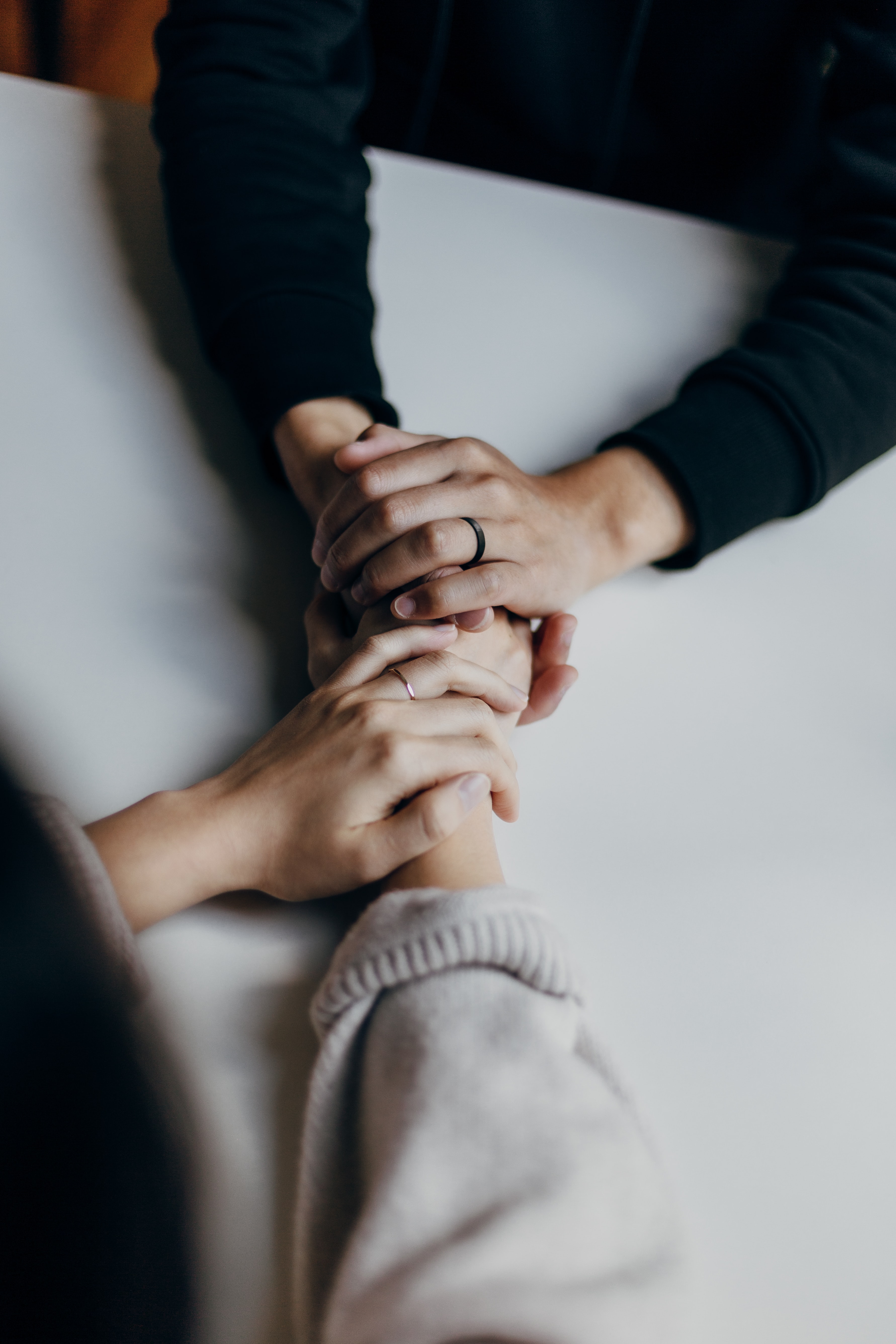 hands from 3 different people reaching in to the center of the image and holding hands