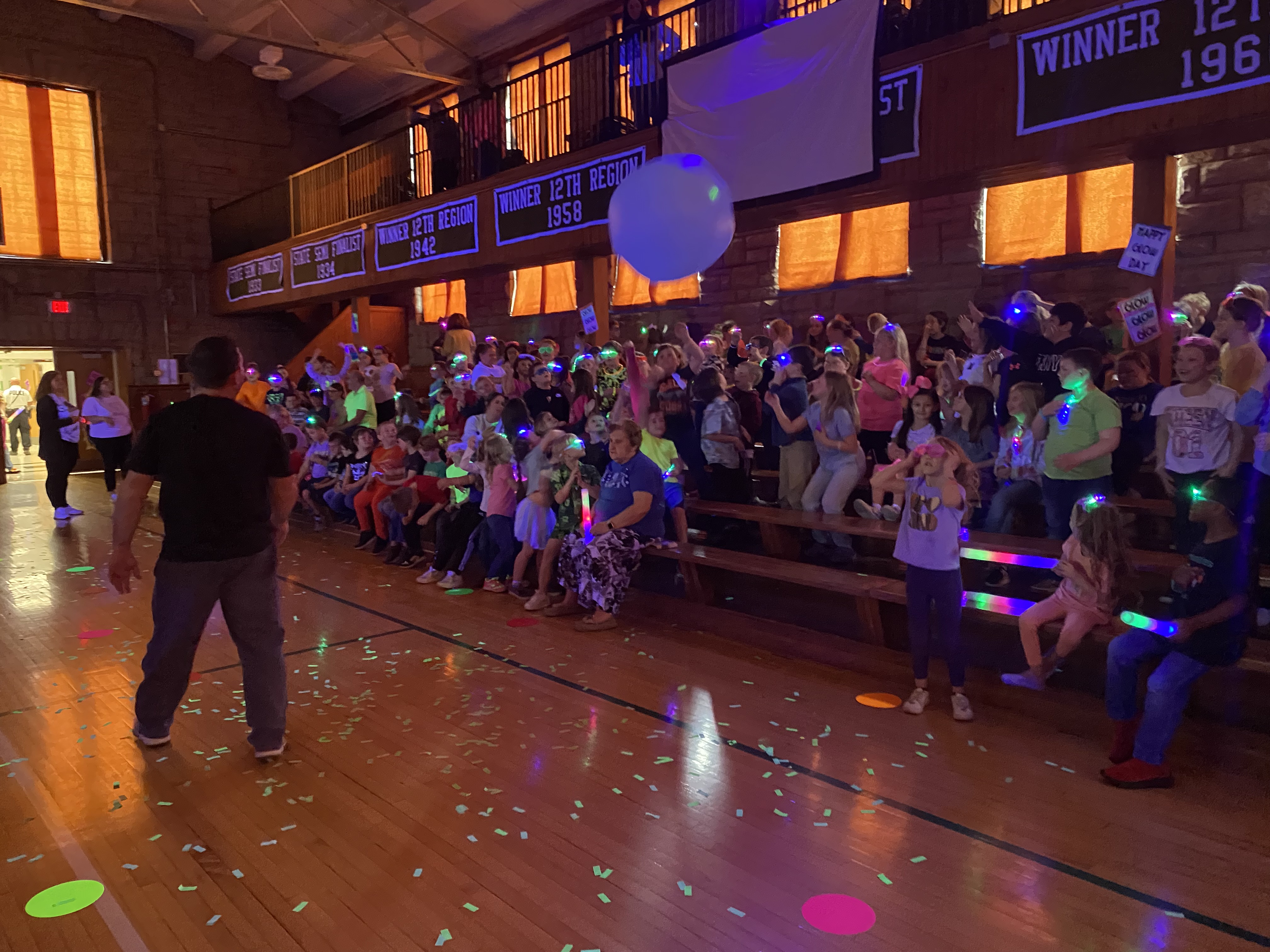 Students in bleachers in a dark room with glow accessories.
