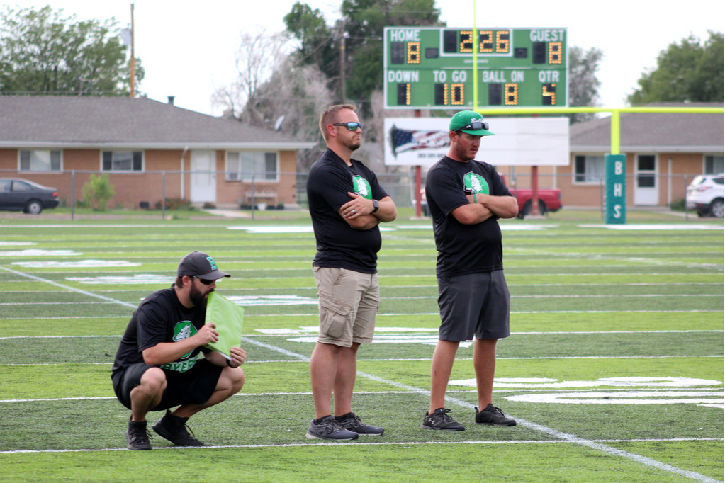 JH FOOTBALL 21-22 3 coaches looking down field trying to figure out the next play.