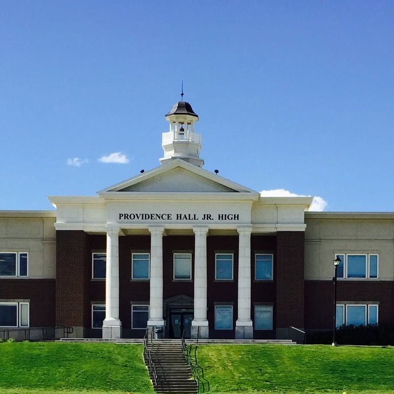Large building with columns and a cupola. Set in a field of green grass. Blue sky and clouds.