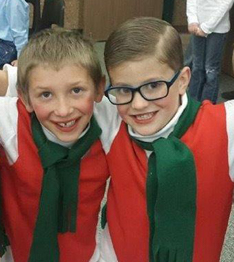 Two small boys, one with glasses, wearing red vests and green scarves