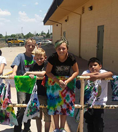 a group of students smiling over a rack of tie-dyed shirts