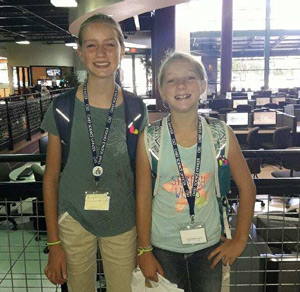 Two girls with nametag lanyards and backpacks smiling