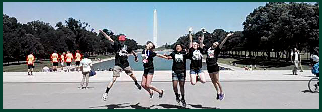 a group of students jumping in the air in front of the reflecting pool and the Washington Monument in Washington, D.C.