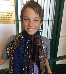 a young boy grinning while wearing at least seven separate neck ties such that they form a kind of monstrous scarf