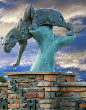 a turquoise statue of a cougar with a clouded sky behind it