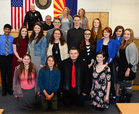 a group of students and teachers smiling in front of flags and the city seal