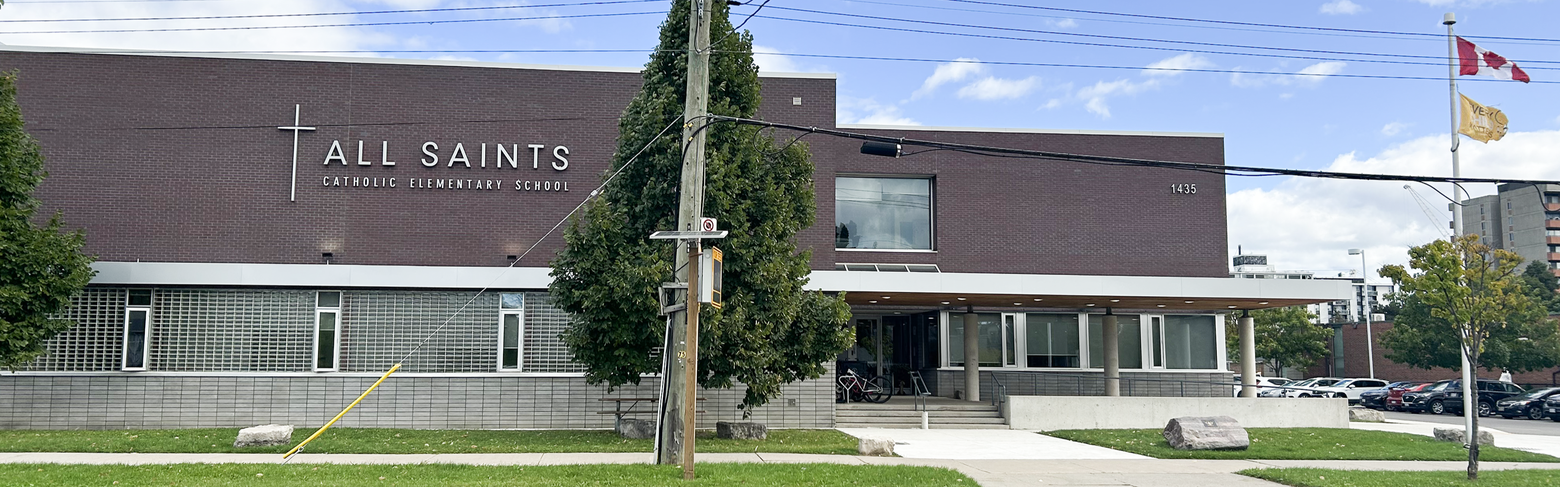 Photo of the All Saints Catholic Elementary School building, showing a modern brick-and-glass building looking out onto the road