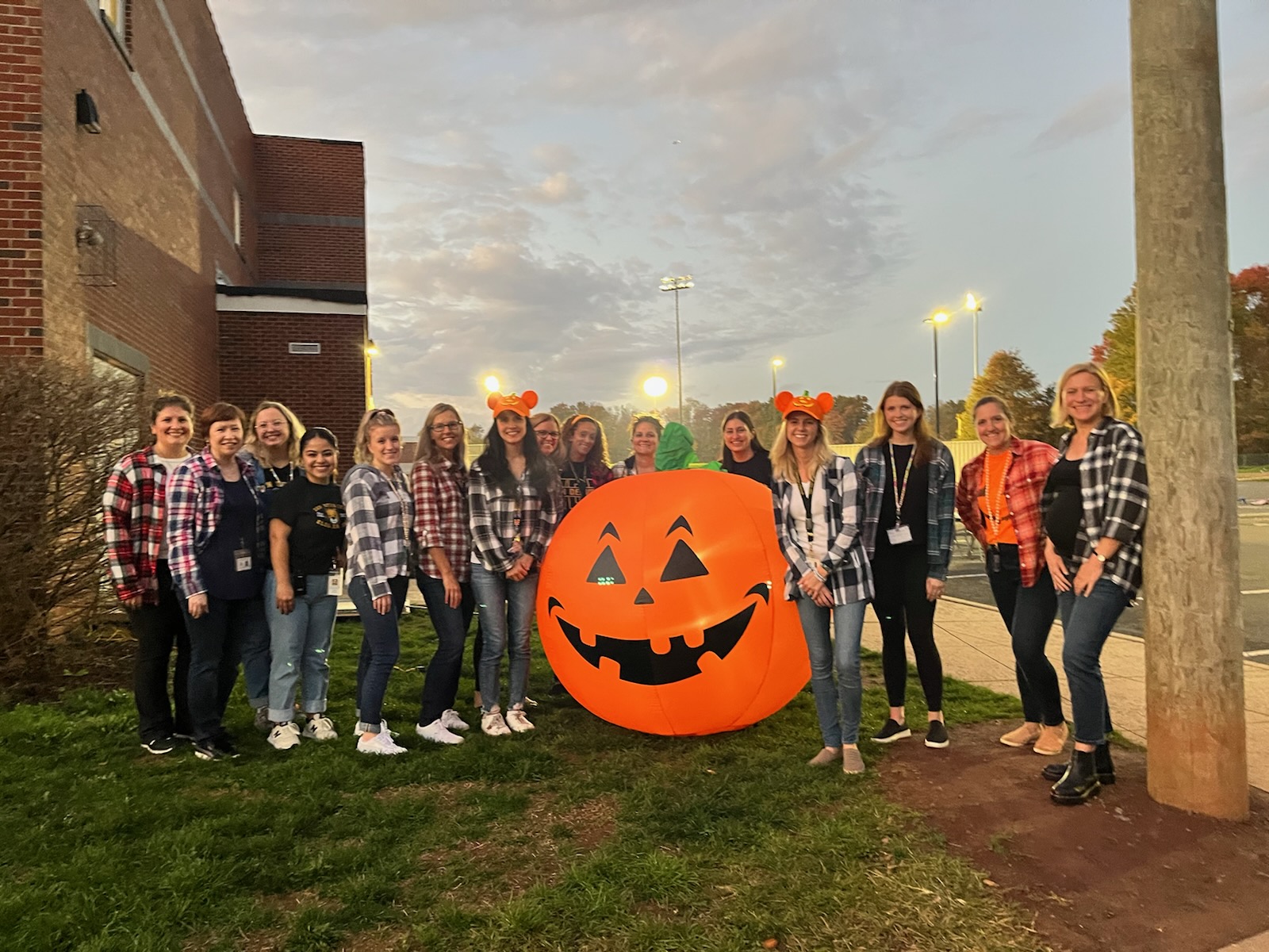 adults in plaid posing for the camera around an orange blow up pumpkin